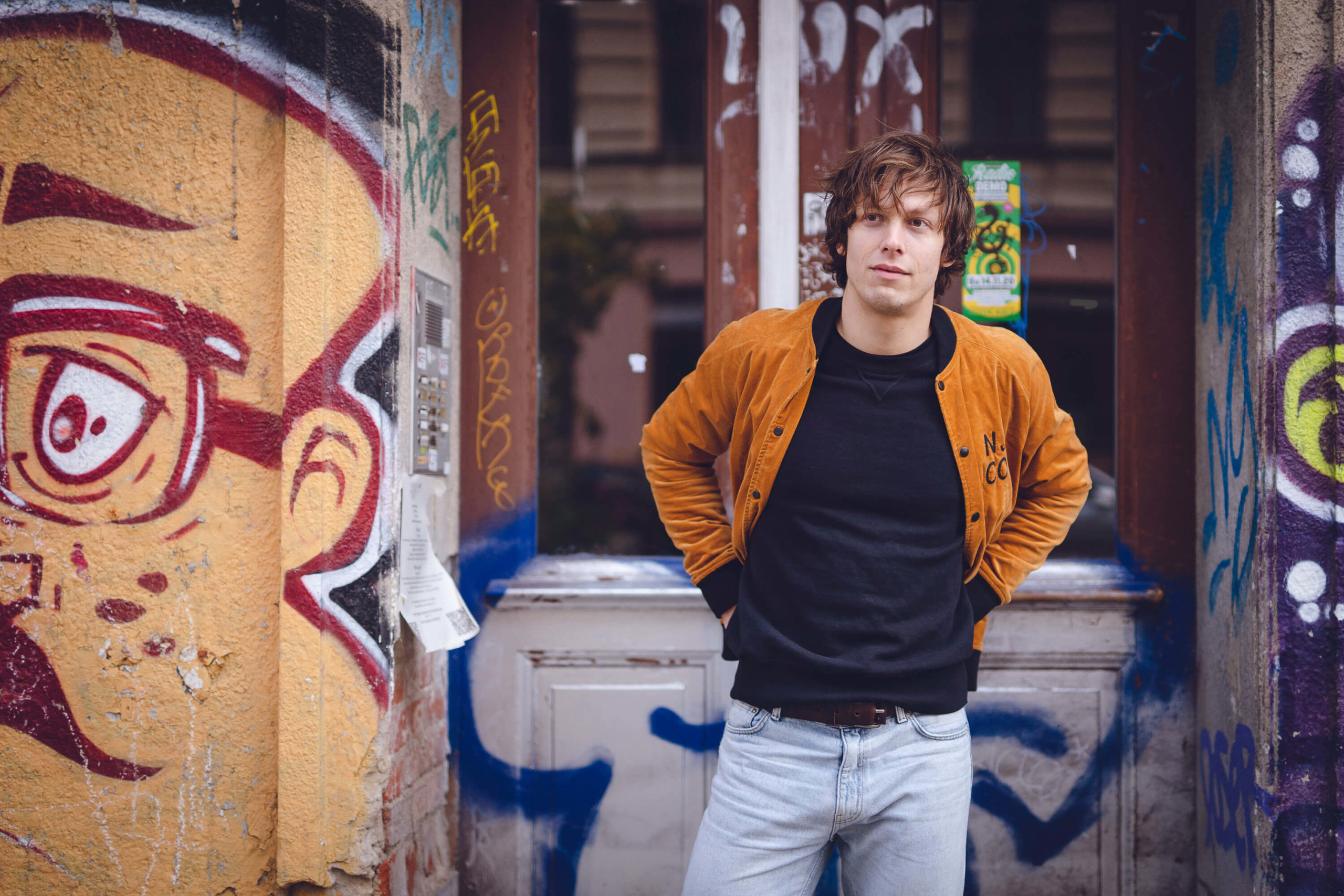 musician Simon Meyer stands in front of house entrance with graffiti wall in Berlin-Kreuzberg